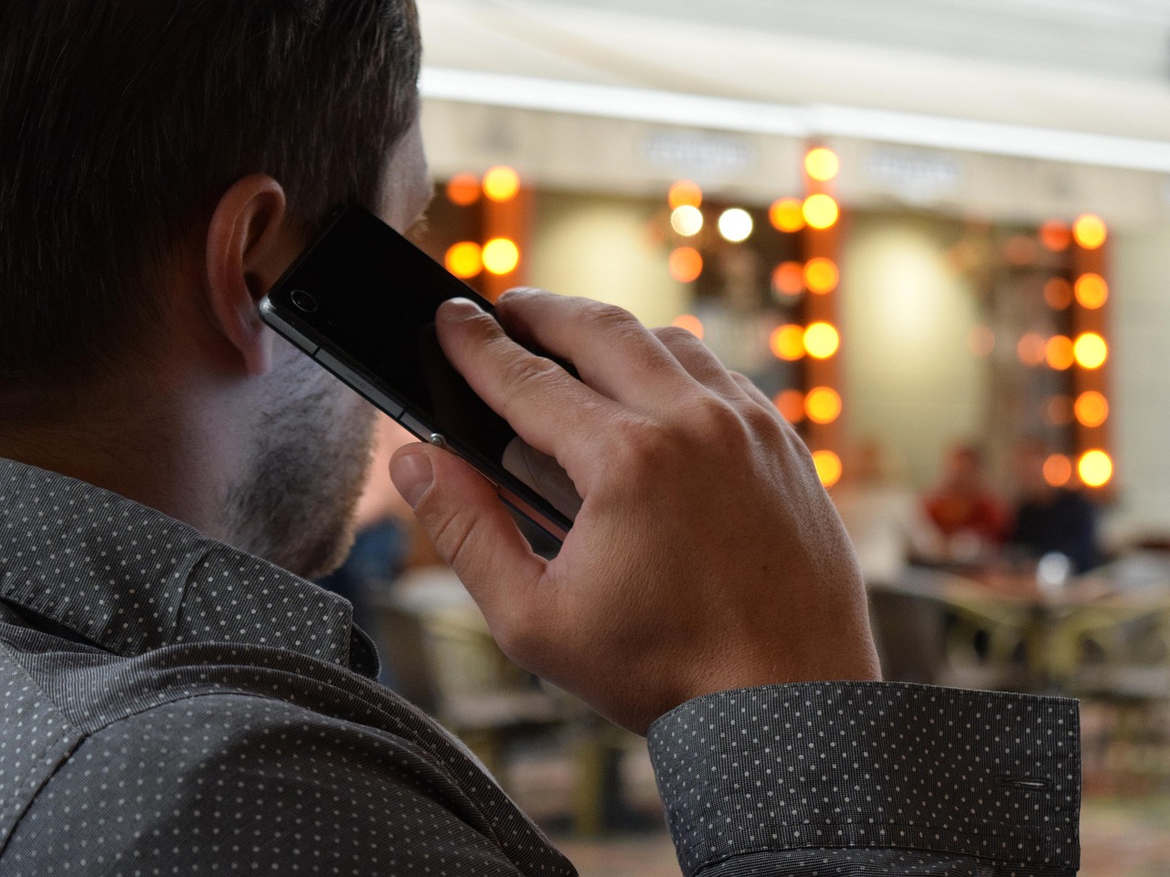 Person on a phone call, seen from behind, with a blurred background of orange lights.