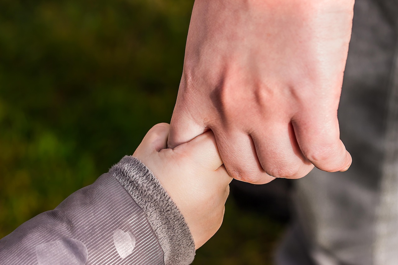 Close-up of an adult hand holding a child's hand outdoors.