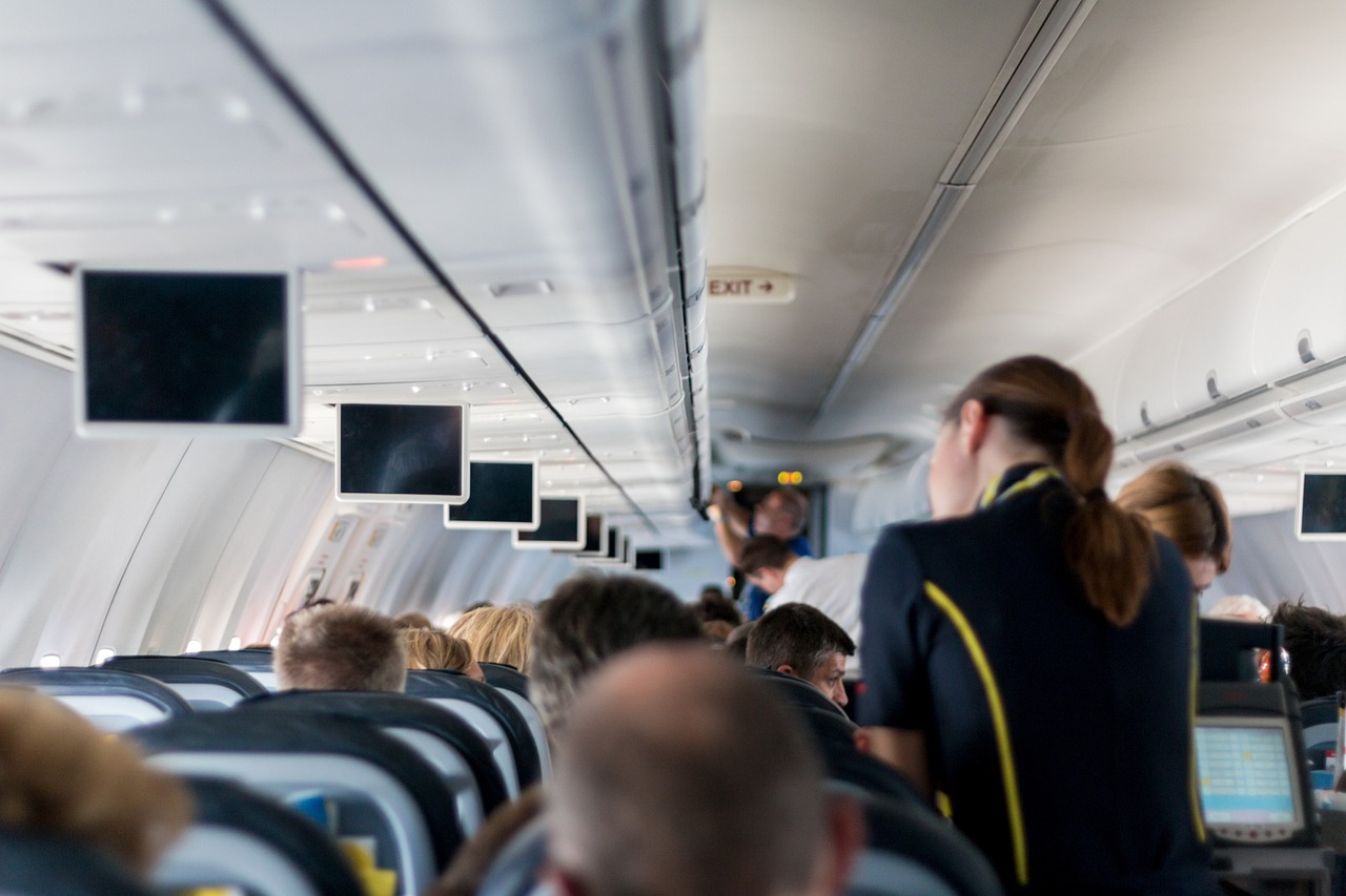Interior of an airplane cabin with passengers seated and a flight attendant walking down the aisle.