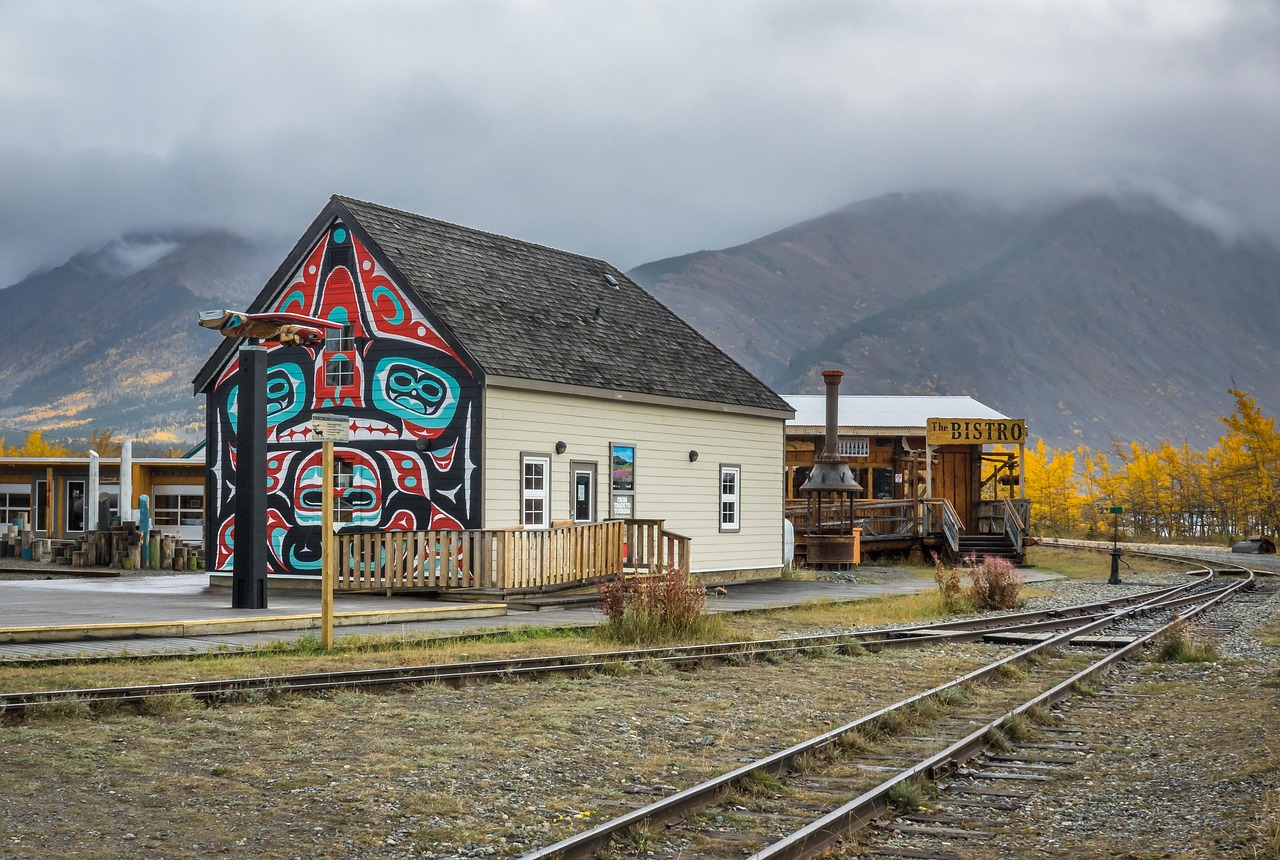 Building with Indigenous-style mural and &ldquo;THE BISTRO&rdquo; sign next to train tracks with mountains in background.