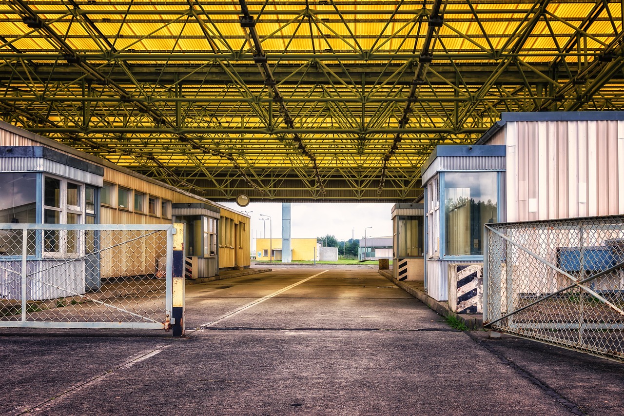 A border crossing with multiple booths under a large yellow metal canopy and open chain-link gates.