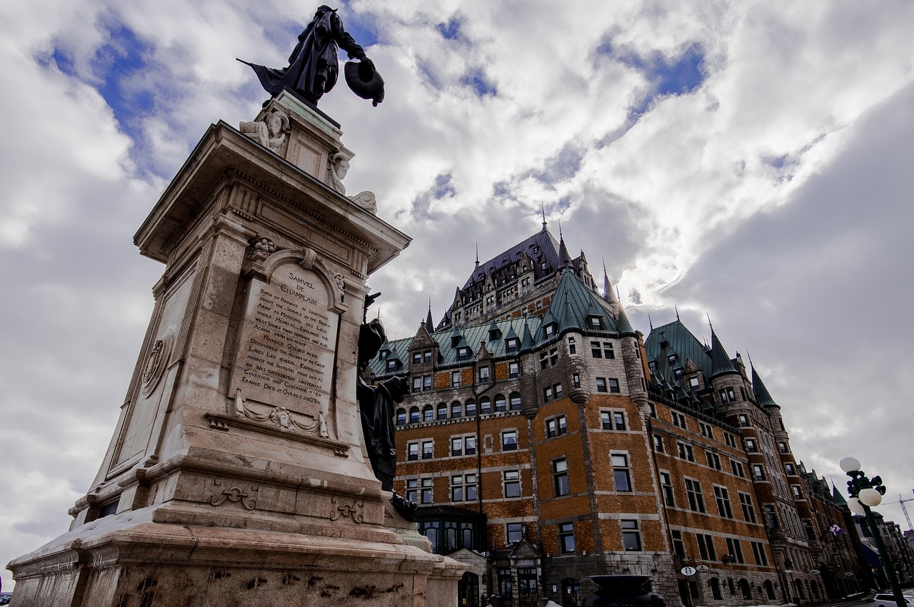 Statue of Samuel de Champlain in front of a grand chateau-style building under a cloudy sky.