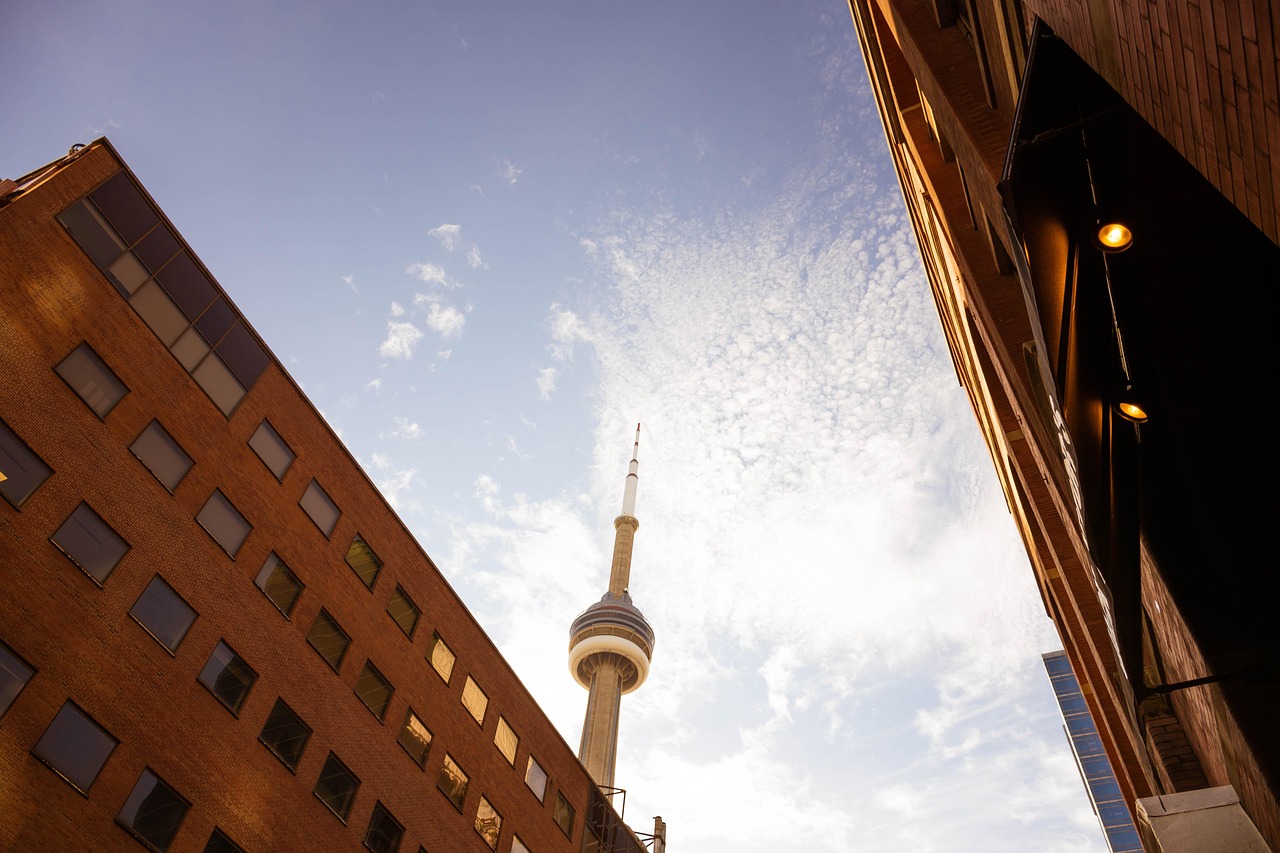 A tall tower with a circular observation deck and antenna, framed by brick buildings against a partly cloudy sky.
