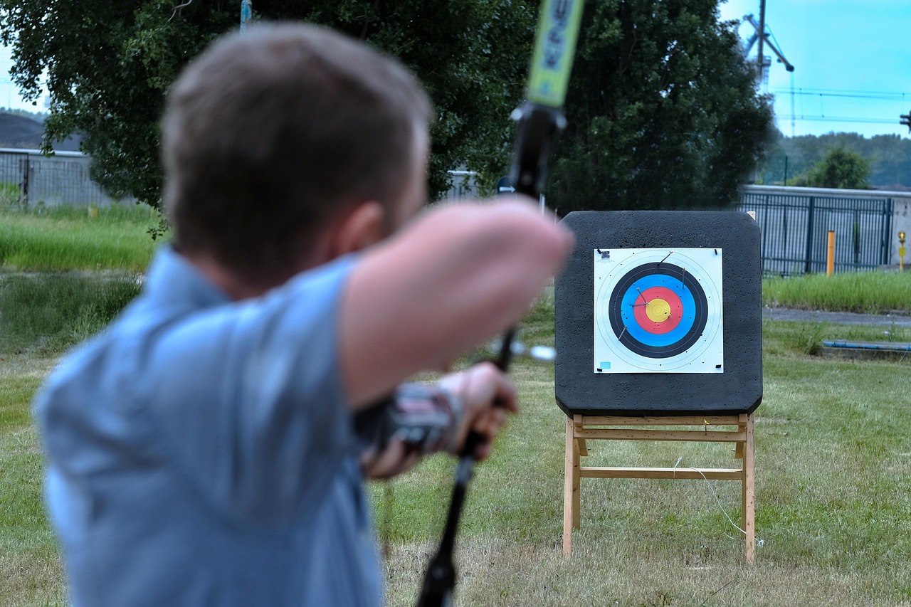 Hand holding darts with one dart in the bullseye of a dartboard.