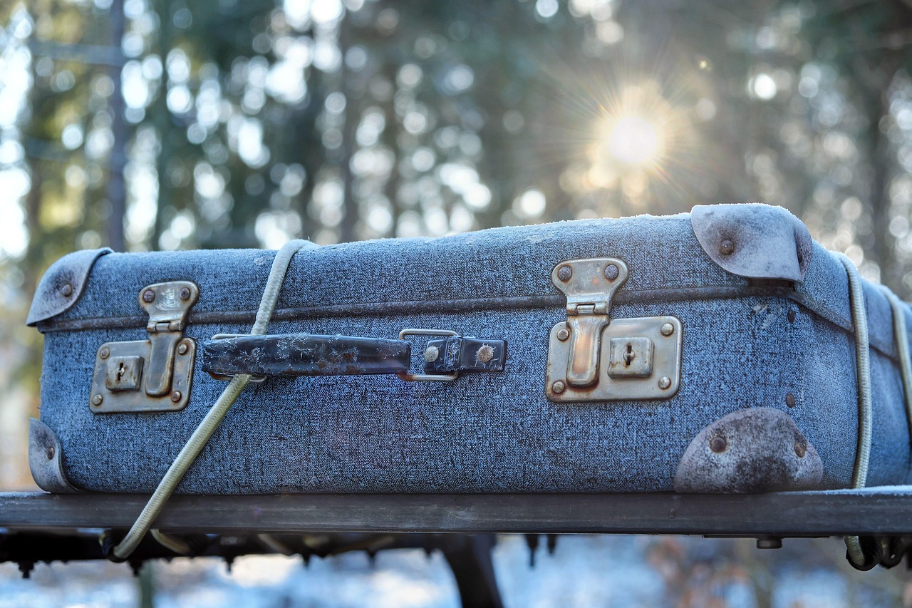 Frost-covered vintage suitcase with a rope, on a roof rack in a blurred winter forest with sunburst.