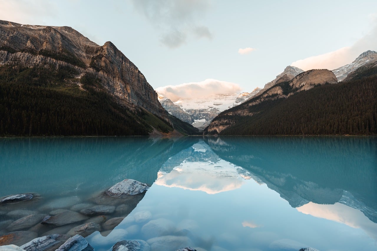 Tranquil turquoise lake reflecting snow-capped mountains and cloudy sky with evergreen forests.
