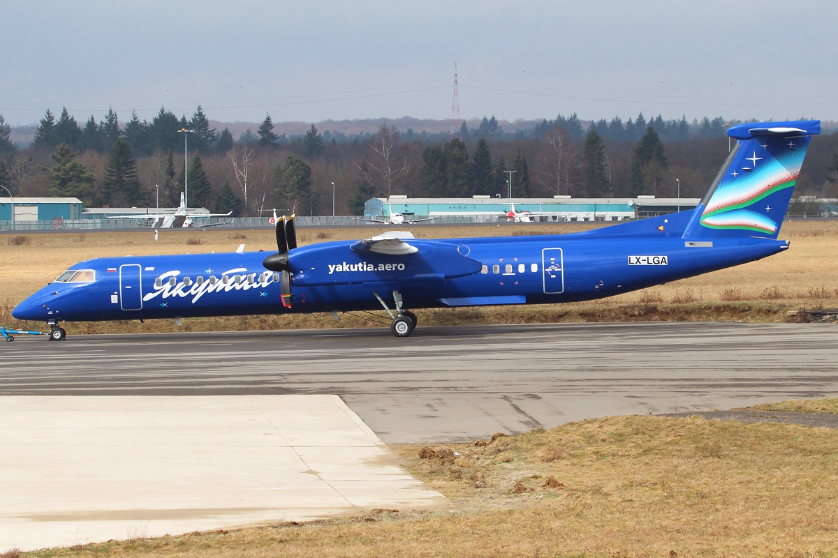 A blue turboprop airplane with 'Yakutia' written on its side and a colorful tail design sits on an airport tarmac.