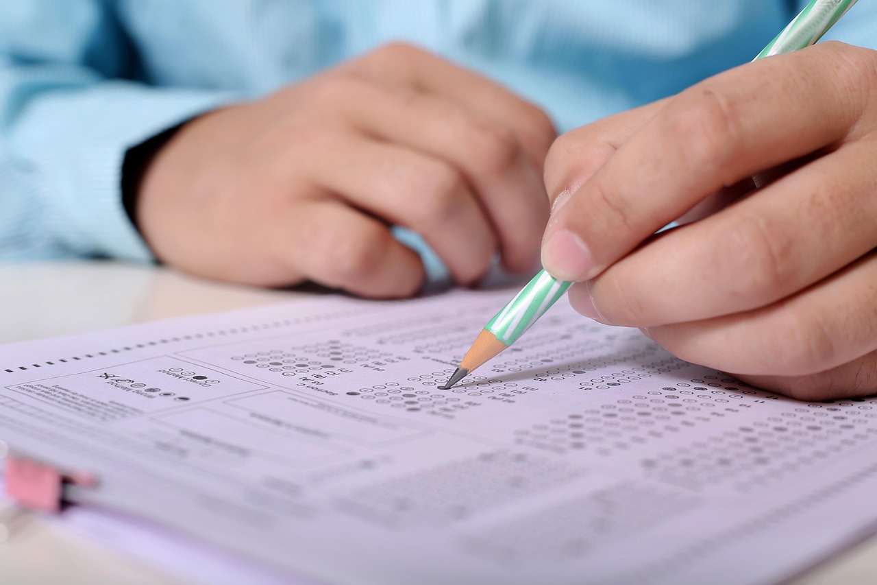 Close-up of hands filling out a multiple-choice answer sheet with a pencil.