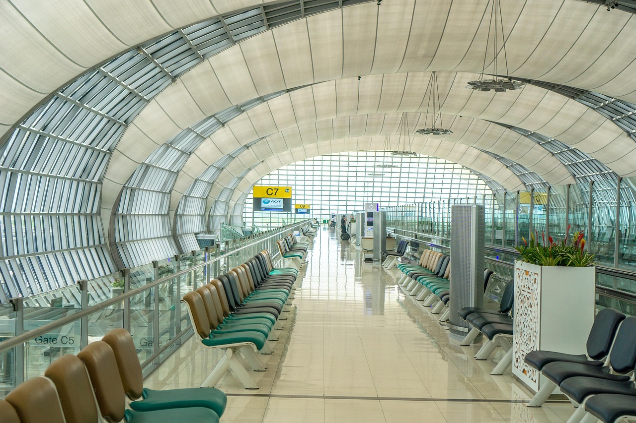 A long, modern airport terminal corridor with rows of empty seats, large windows, and a curved ceiling.