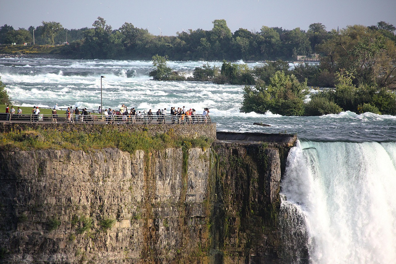 People on a walkway overlooking a large waterfall and turbulent river.