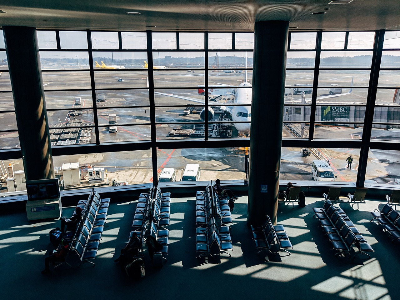 An airport waiting area with rows of seats looking out through large windows at a parked airplane.