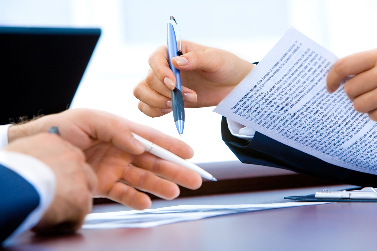 Two people's hands, one holding a pen, the other holding a document with text.