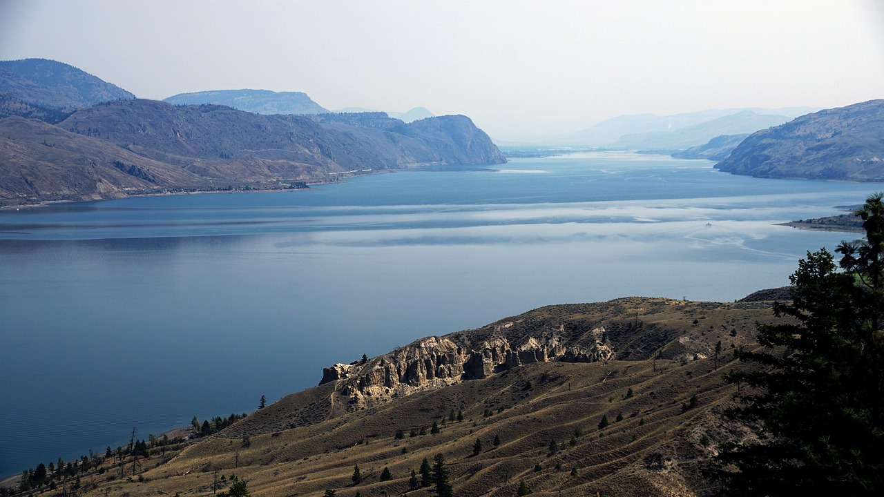 Hazy landscape of a wide lake or river winding through dry, rocky hills.