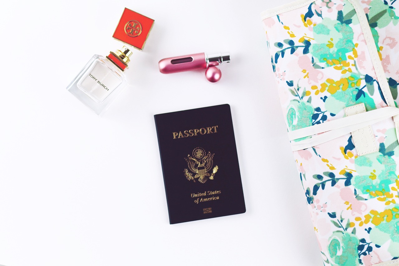 A dark blue United States passport, a perfume bottle, a perfume atomizer, and a floral travel bag on a white surface.