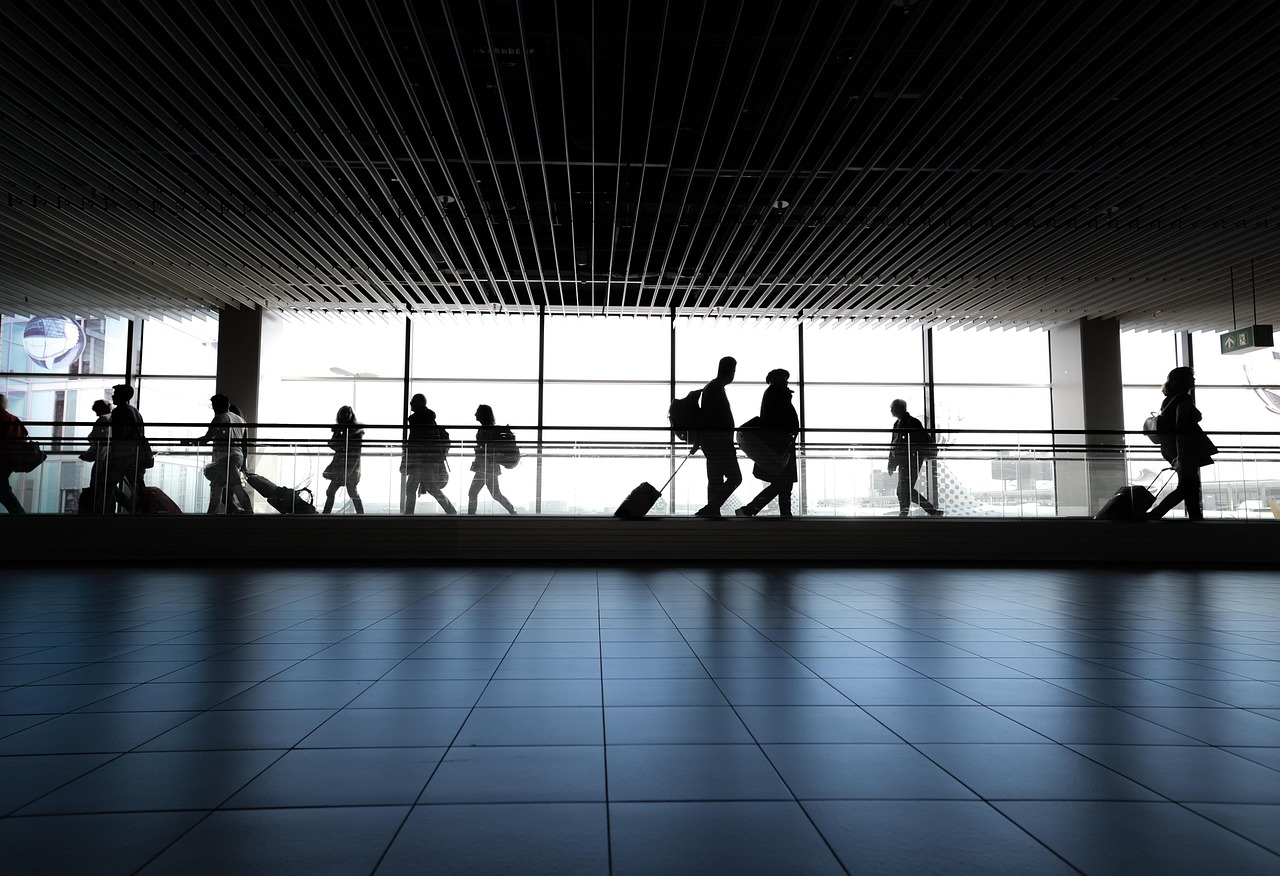 Silhouettes of travelers with luggage walking through a bright airport terminal.