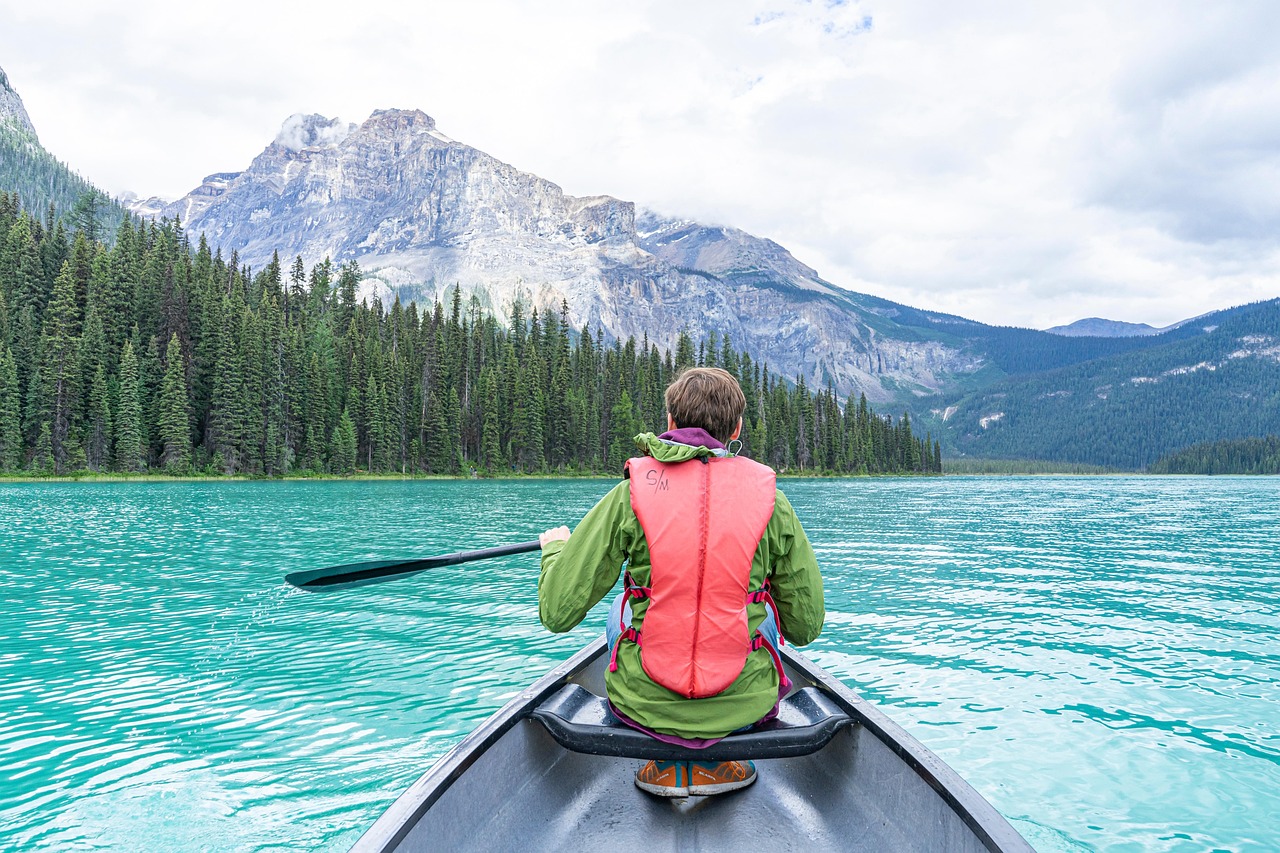 Person canoeing on a turquoise lake surrounded by mountains and forests.