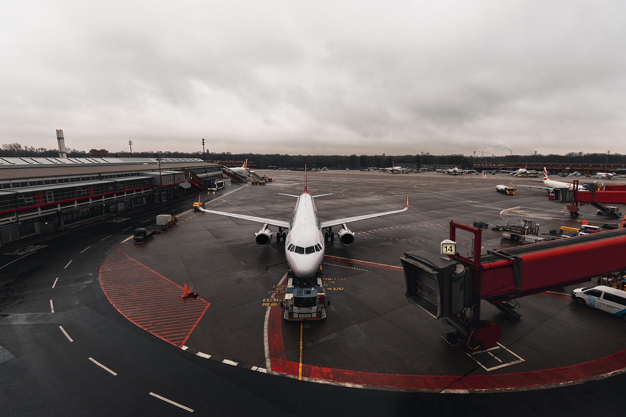 Overhead view of a white passenger jet on a wet airport tarmac under a cloudy sky.
