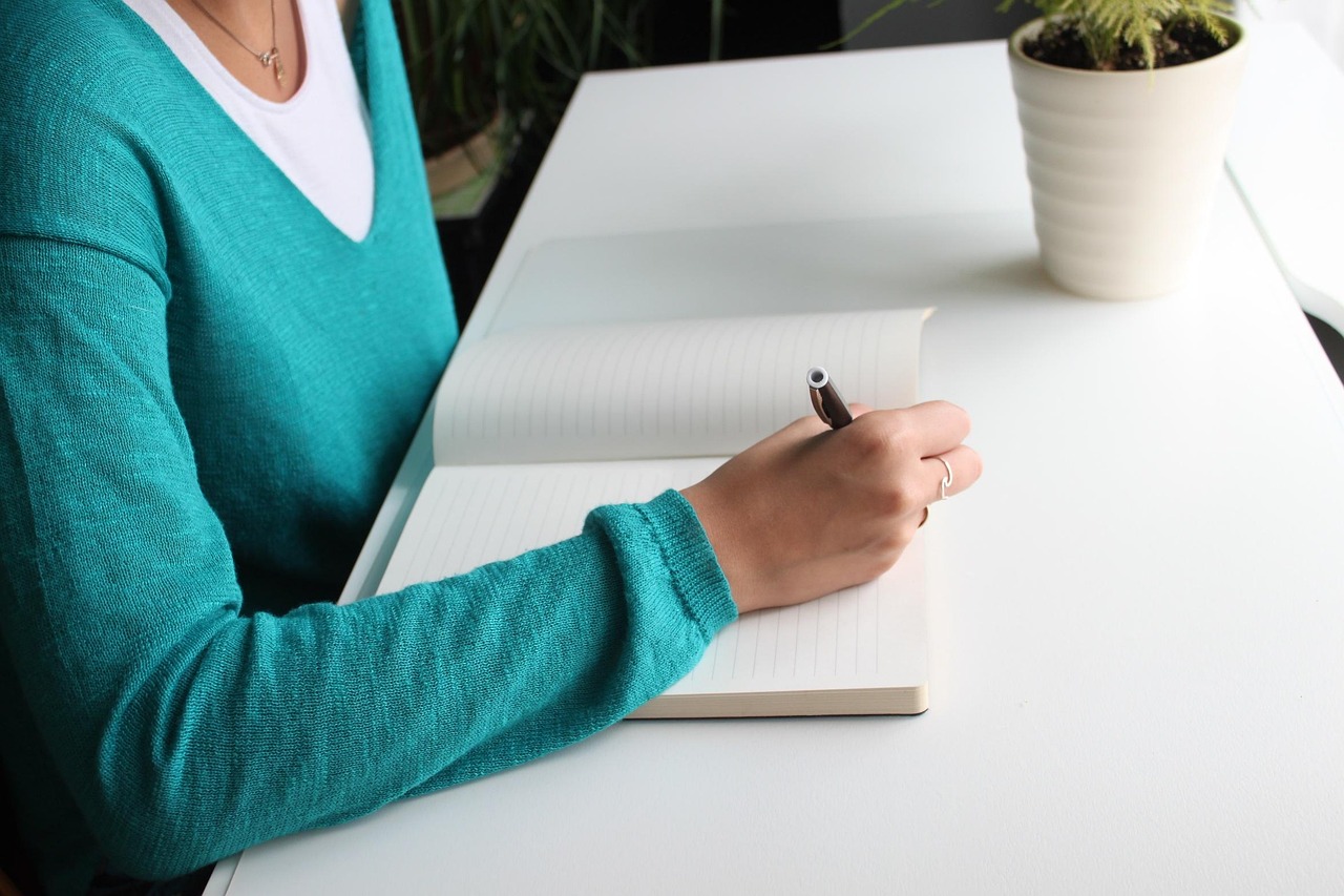 Person writing in a blank notebook on a white desk.