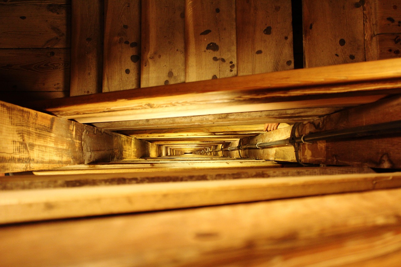 Low-angle view looking up a narrow, square wooden shaft with ladder-like steps, illuminated by warm light.
