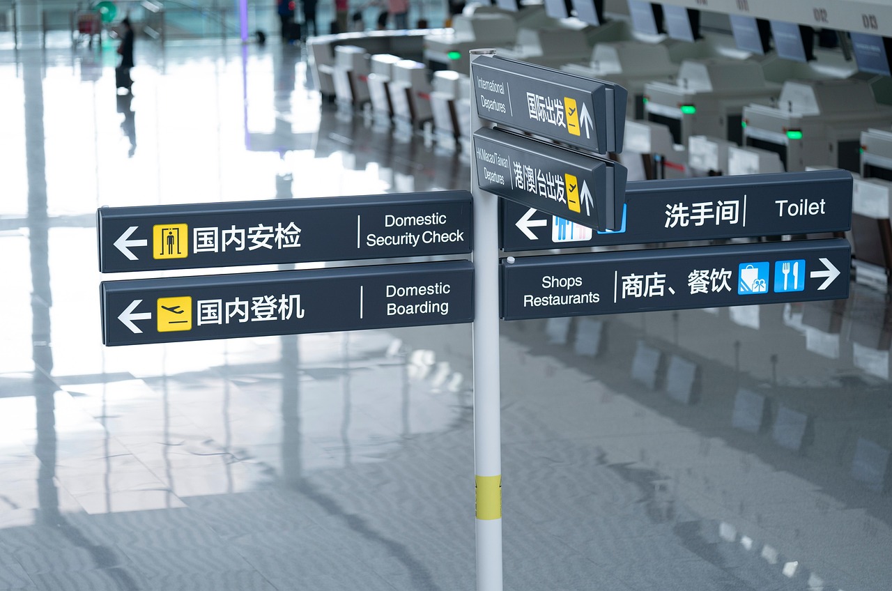 Airport directional signpost with English and Chinese text for security, boarding, departures, shops, restaurants, and toilet.