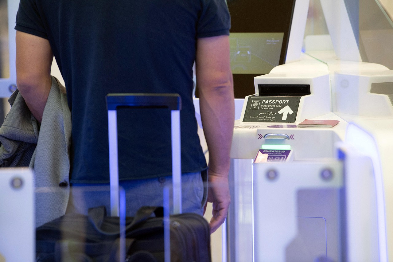 A person at an automated passport control gate with a suitcase, with signs for 'PASSPORT' and 'EMIRATES ID'.