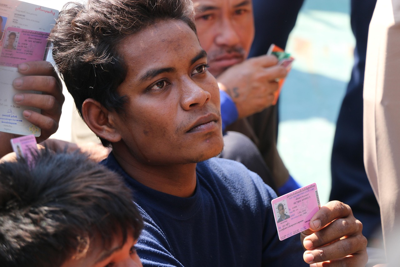 Young man holding a pink identification card with a photo, with other documents visible in the background.