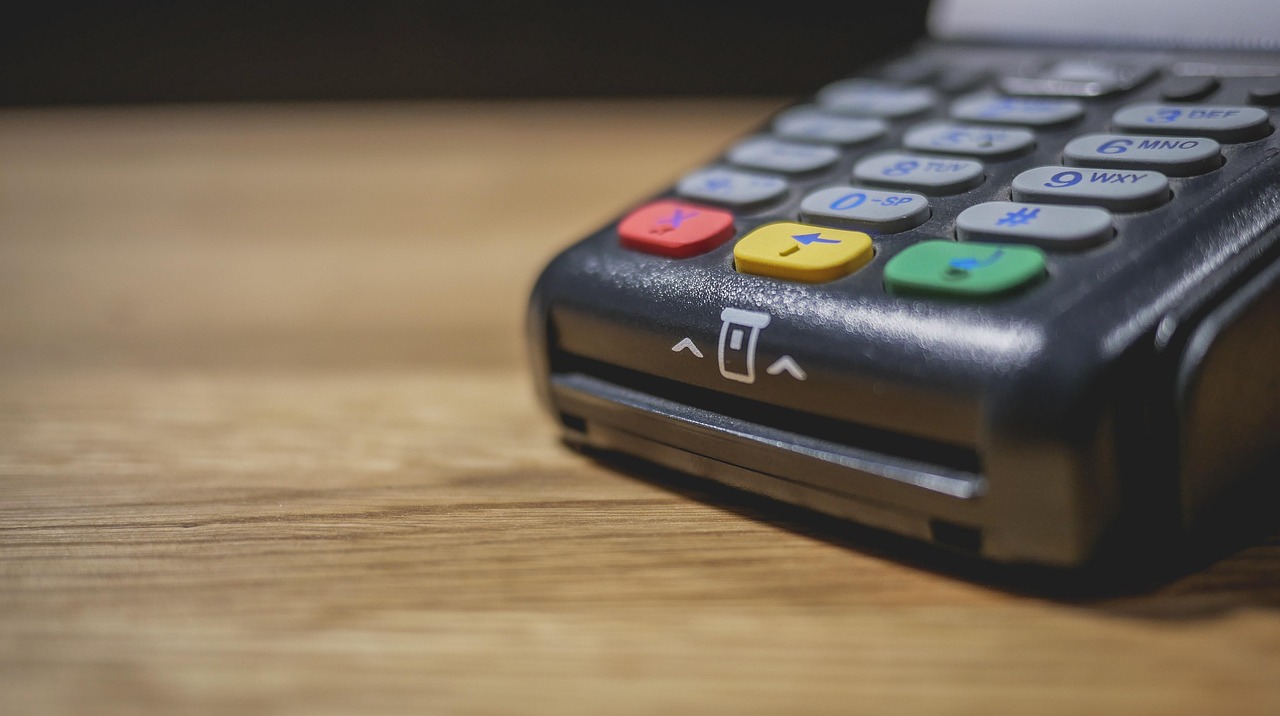 Canada eTA price in your currency: a card payment terminal in close-up on a warm wooden counter with a soft blurred background