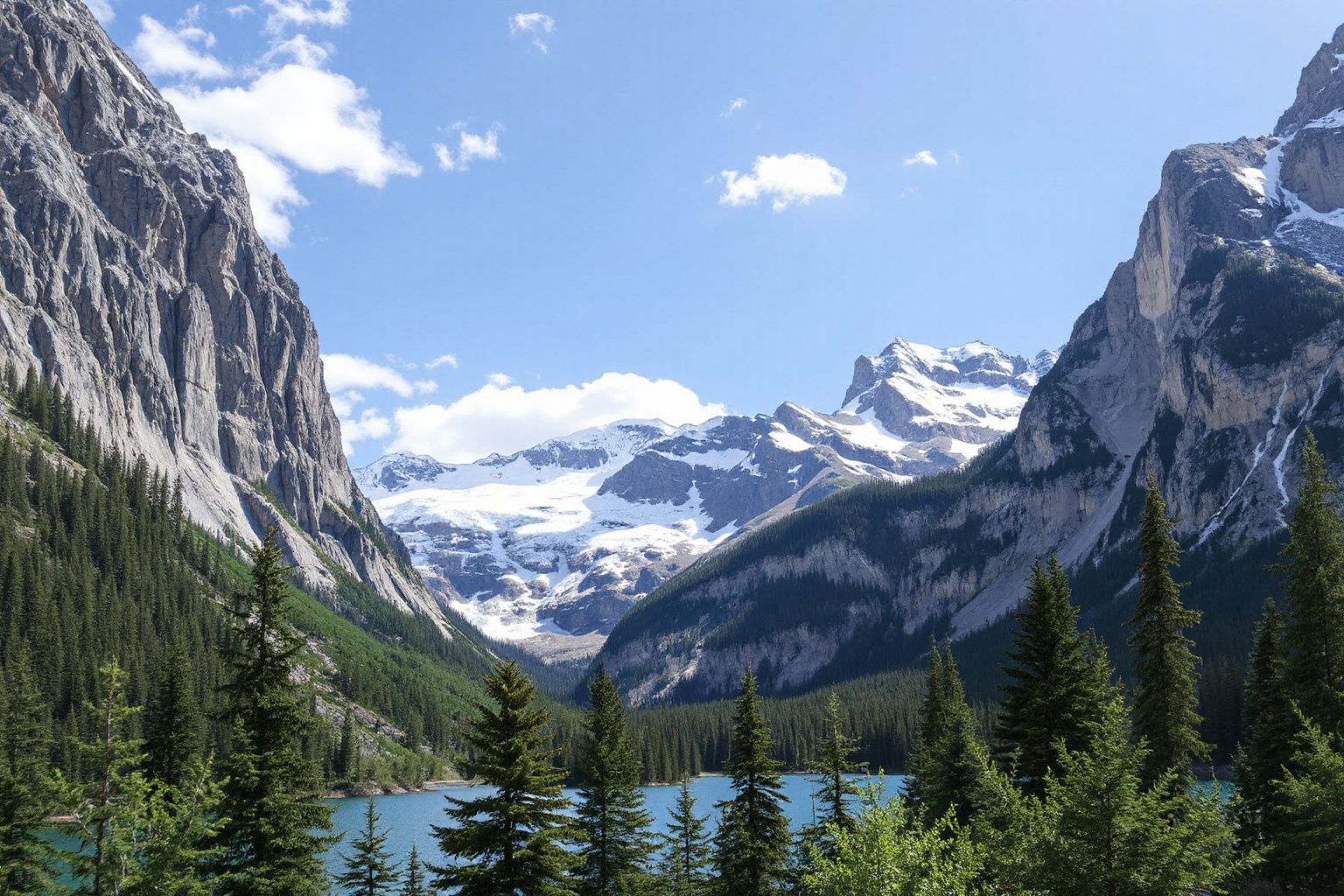 A clear blue lake surrounded by green pine trees and towering grey mountains with snow-capped peaks under a blue sky.