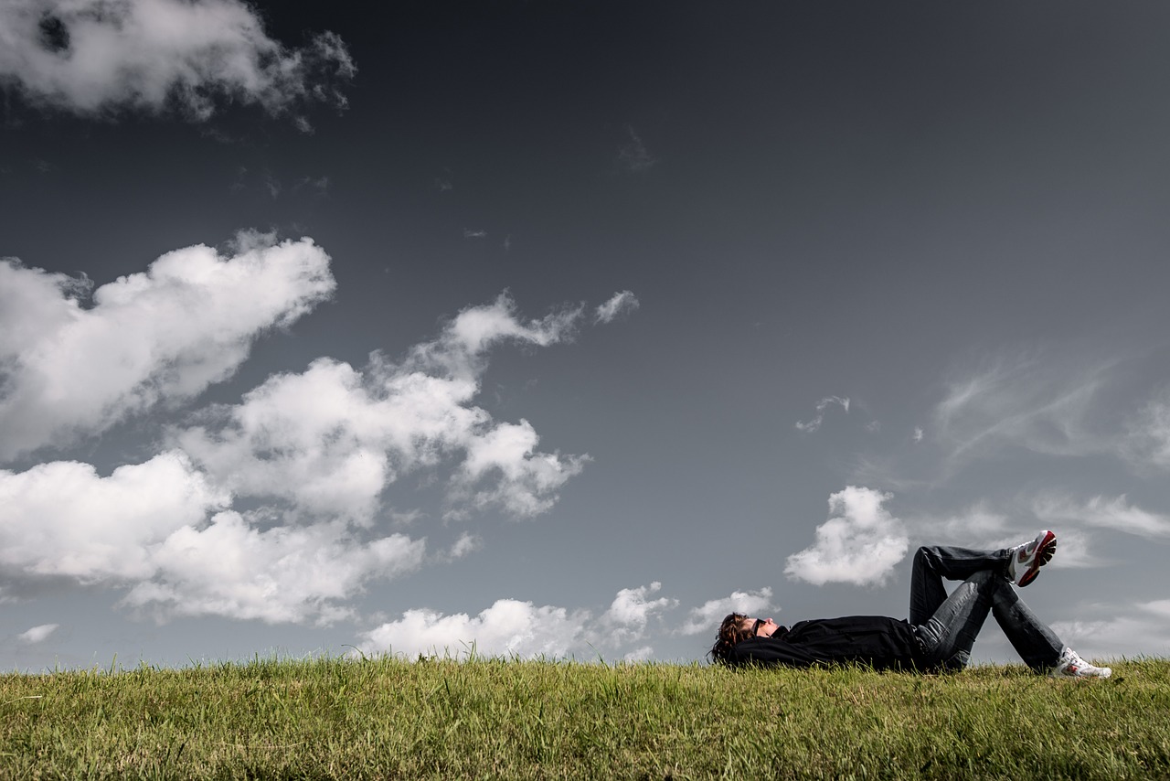 Person lying on their back on a grassy hill, looking up at a dark cloudy sky.