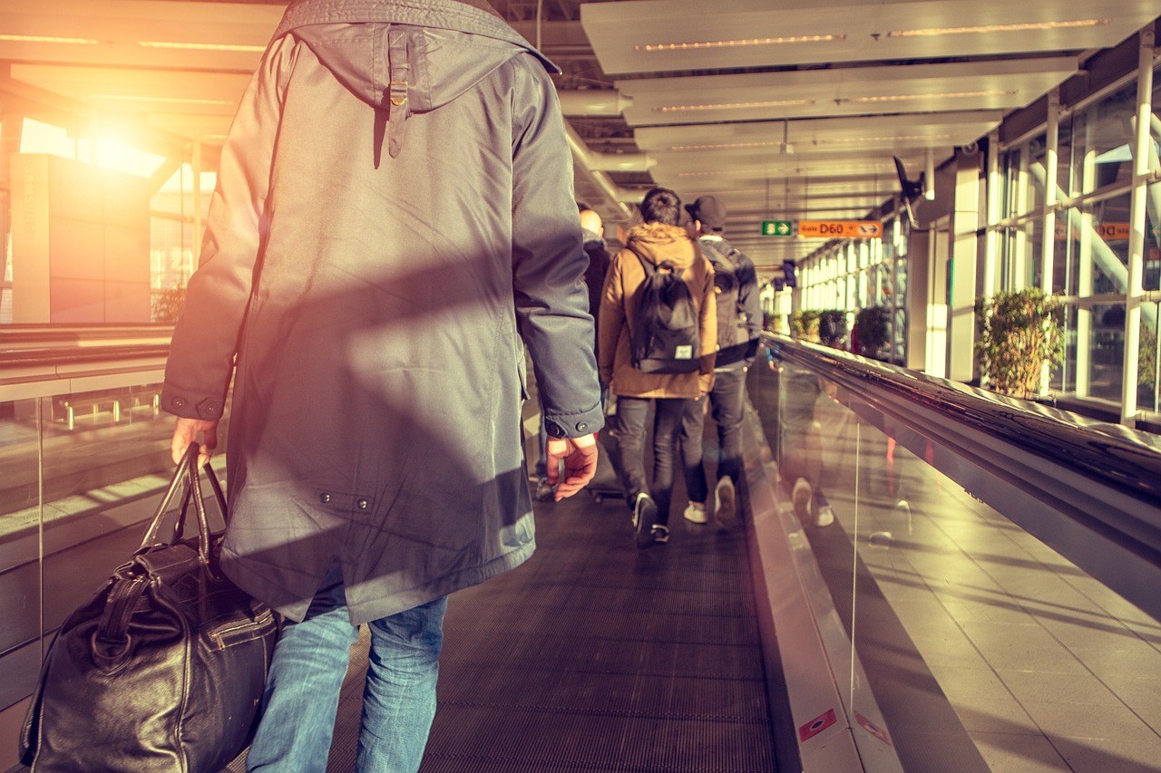 Person walking on a moving walkway in a bright airport terminal with other passengers and signs.