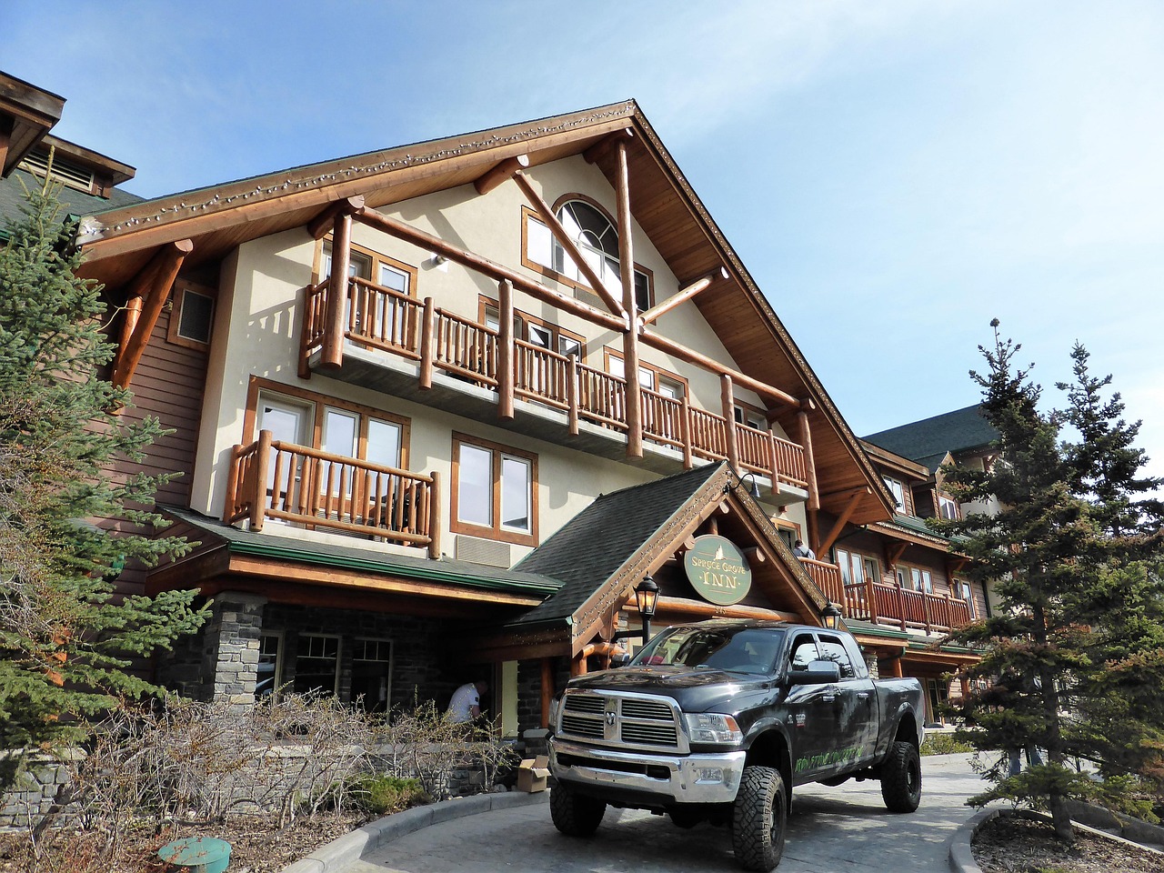 Rustic lodge or hotel building with wooden beams, balconies, pine trees, and a black pickup truck.