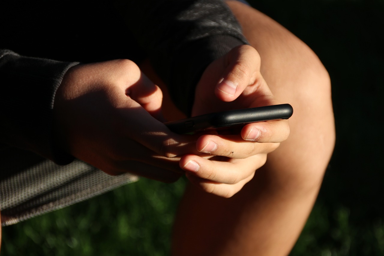 Close-up of hands holding a black smartphone, with fingers poised over the screen.