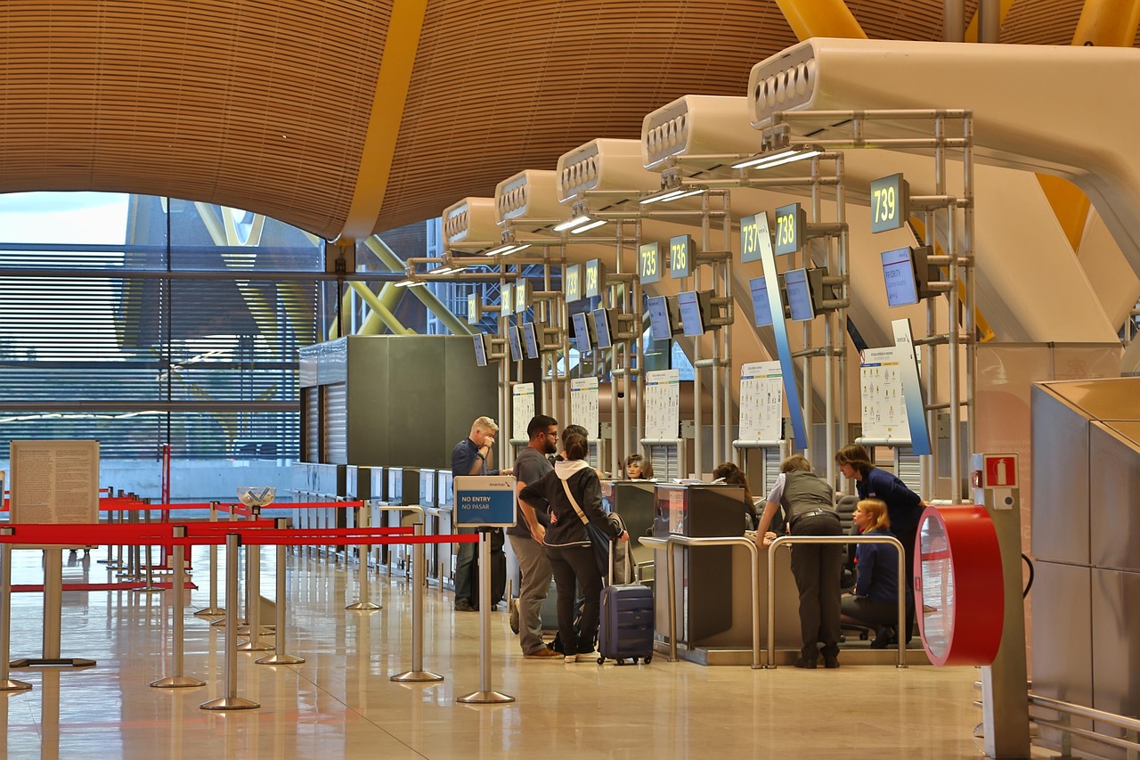 People queue at airport check-in counters with digital screens and a modern wooden ceiling.